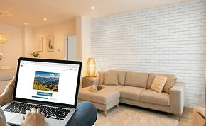 Person using a laptop in a modern living room with a sectional sofa and coffee table.